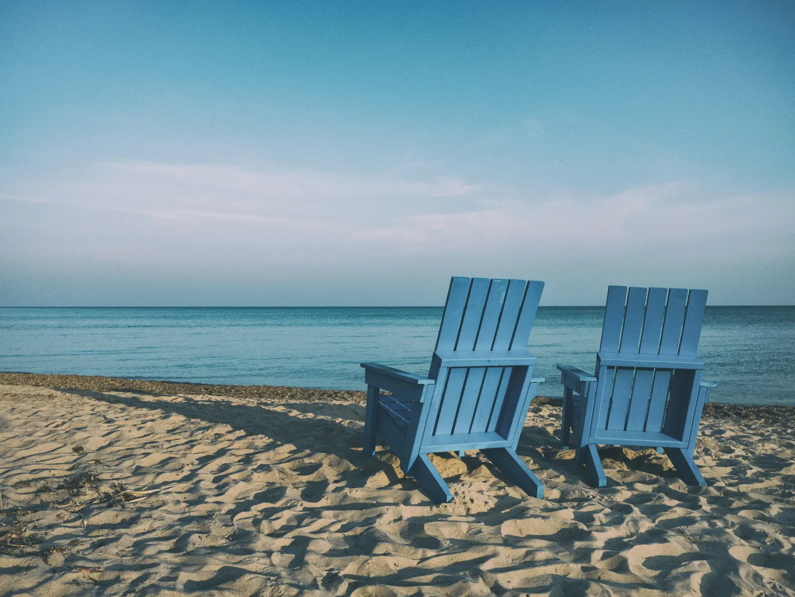 Two blue chairs facing the sea on a quiet beach