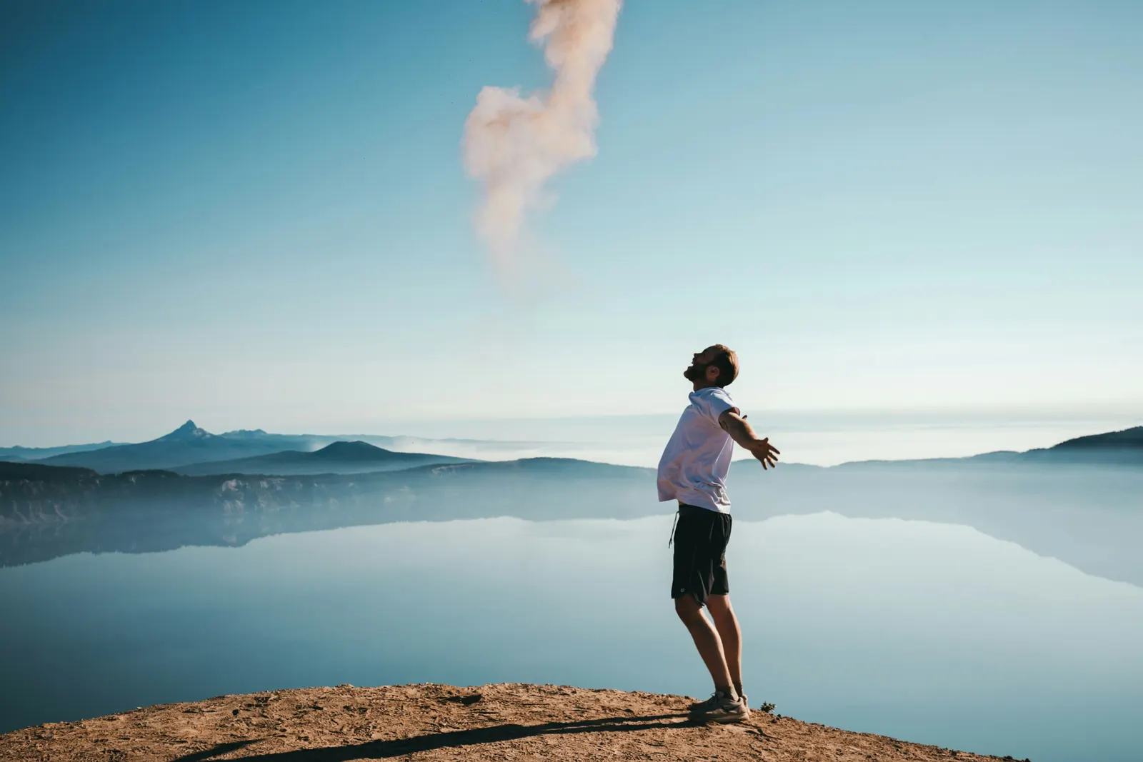 Man with arms open above a misty lake